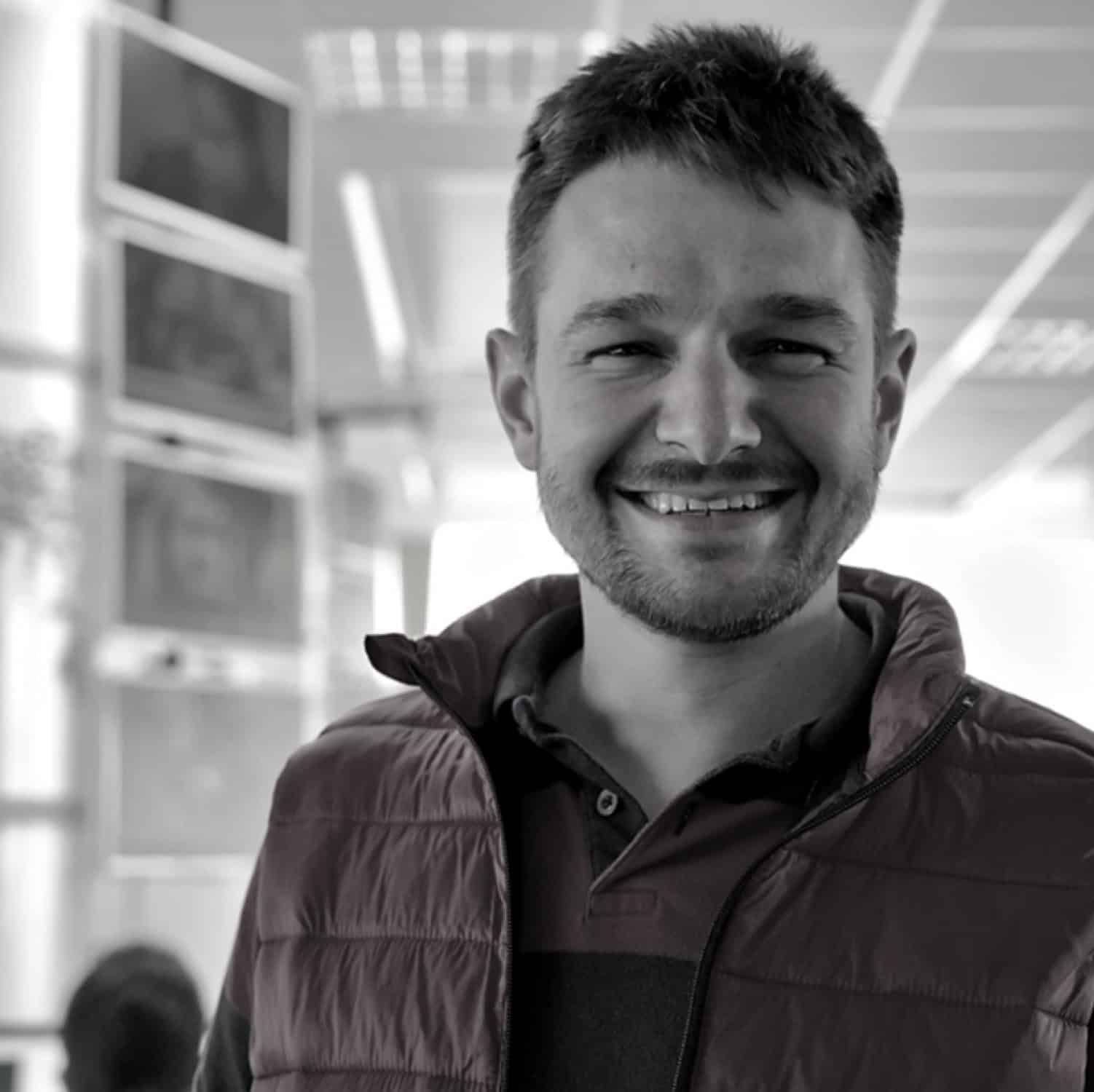 Close-up of a smiling man in an indoor setting with architectural elements.