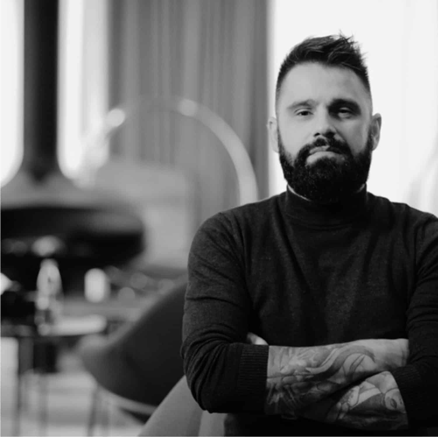 Man with tattooed arms in a modern workspace, blueprint background.